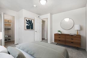 Jackson apartment for rent - A bedroom with a grey bed, a wooden dresser and walk-in closet at Trillium Pointe Apartment Homes, Jackson, MI