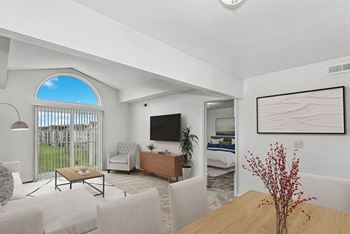 A living room with a television, a couch, a chair, a coffee table, and a bed in the background