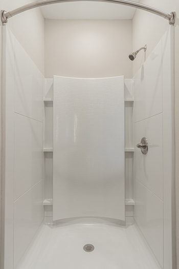 A walk in shower with white tile and a white shower curtain
