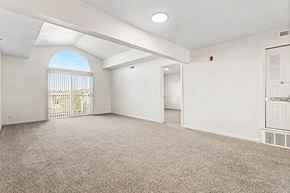 Elkhorn apartment for rent - A spacious living room with a cathedral ceiling, carpeted floor and a sliding glass door to a balcony at West Hampton Park Apartment Homes, Nebraska, 68022