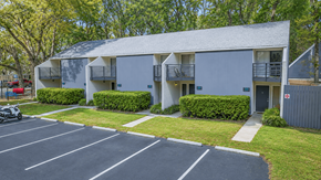 Gainesville townhouse for rent - A parking lot in front of a grey building with trees in the background.