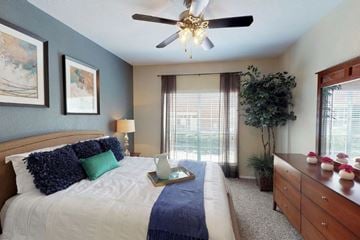 Tulsa apartment for rent - A bedroom with a bed, a ceiling fan, and a nightstand with flowers.