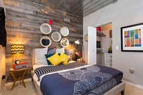Ann Arbor apartment for rent - a bedroom with a bed with blue and yellow pillows and a reclaimed wood wall at Ann Arbor City Club, Ann Arbor Michigan