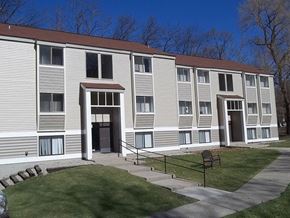 Brighton apartment for rent - Exterior of building from the parking lot.  Sidwalk runs horizontal to building and there are 2 entrance doors.  Each door has white pillars on each side.  Building has beige siding with white trim.  Grass is green.
