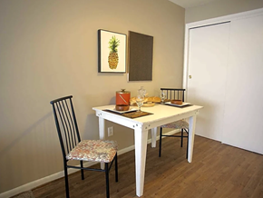 Columbus apartment for rent - Dining Area with white table and 2 cloth covered rod iron chairs.  Pineapple photo above table on dark wood floor.  White doors behind table on right wall.