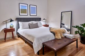 Detroit apartment for rent - a bedroom with a large bed with white bedding and a brown leather bench at the end