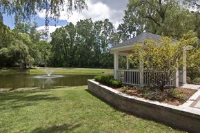 Brighton apartment for rent - White gazebo to the right of photo with trees, greenery and lined with wood surround.  Green grass in the middle leading up to a pond with a fountain.  Sky and green trees in the background.