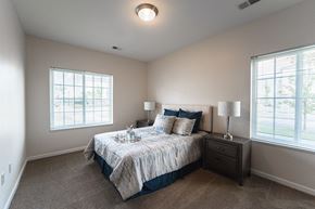 Shelby Township apartment for rent - Bedroom, large bed in center of room with matching end tables on each side, window to the left and to the right of the bed, light tan painted walls with tan carpet.