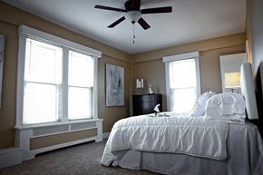 Detroit apartment for rent - Primary bedroom with plush bed, carpeting, large windows, and a ceiling fan.