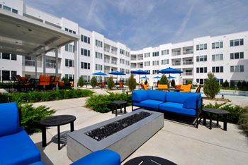 A patio with couches tables and umbrellas in front of an apartment building