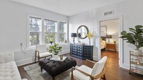 Detroit apartment for rent - A living room with a black ottoman, white chair, and a large window.