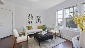 Detroit apartment for rent - A living room with a white couch, a black ottoman, and a rug.