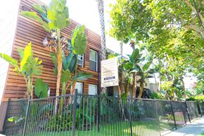 Los Angeles apartment for rent - side view of building with leasing sign, gate, and grassy area.