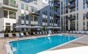 Raleigh apartment for rent - A swimming pool with lounge chairs and umbrellas in front of a modern building.