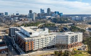 Raleigh apartment for rent - A large white building with a lot of windows is in the foreground of a cityscape.