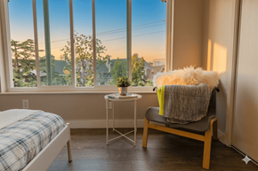 Oakland apartment for rent - A cozy bedroom with a bed, chair, and a view of the neighborhood through the window.