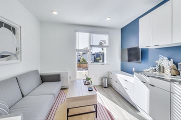 Oakland apartment for rent - A modern living room with a grey sofa and a kitchen area with white cabinets.