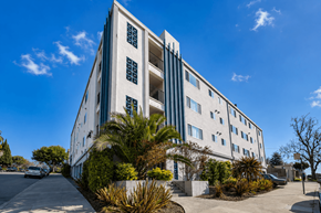 Oakland apartment for rent - A white building with blue trim and windows is surrounded by greenery and a clear blue sky.