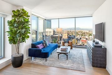 Oakland apartment for rent - A living room with a blue couch and a large window overlooking the city.