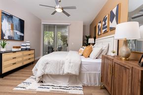 Las Vegas apartment for rent - Spring Valley, NV, 89147 Apartments for Rent - Alicante - Inviting Bedroom With Cozy Bed, Ceiling Fan, Wood Dresser, And Sliding Glass Door With Vertical Blinds Leading To Private Patio.