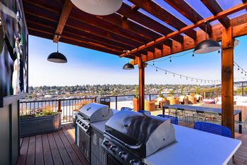 A grill is on a wooden deck with a city view in the background.