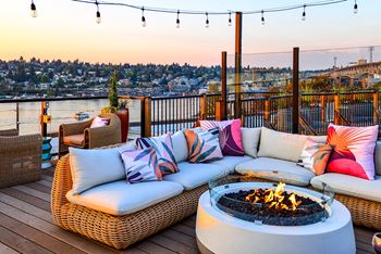 A patio with a fire pit and couches overlooking a cityscape at dusk.