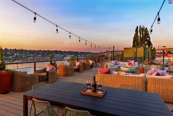 A rooftop patio with a table and chairs overlooking a cityscape at dusk.