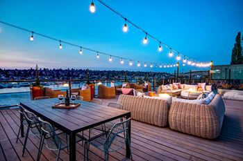 A wooden table with chairs and a couch on a deck with string lights.