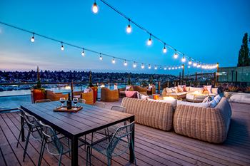 A wooden table with chairs and a couch on a deck with string lights.