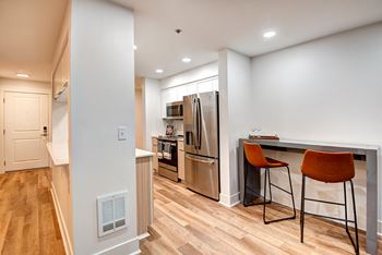 A kitchen with a refrigerator, oven, and bar stools.