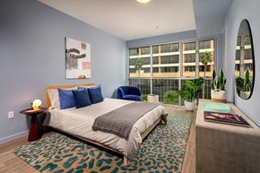 Los Angeles apartment for rent - A bedroom with a bed, a blue chair, a rug, a potted plant, and a mirror.