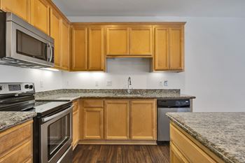 An empty kitchen with granite counter tops and wooden cabinets