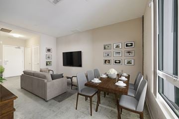 Long Beach apartment for rent - A living room with a grey couch, a wooden dining table with grey chairs, and a flat screen TV mounted on the wall.