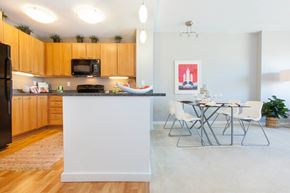 Oakland apartment for rent - A kitchen with wooden cabinets and a white island with a dining table and chairs at The Grand Apartments, Oakland, California