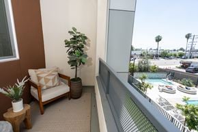 Monrovia apartment for rent - A chair with a pillow and a potted plant sit on a balcony overlooking a pool.