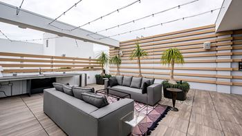 A modern outdoor seating area with grey couches and a wooden floor.