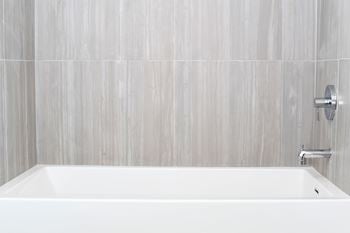A white bathtub in a bathroom with grey tiled walls.