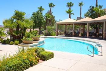 A pool surrounded by palm trees and a patio area.