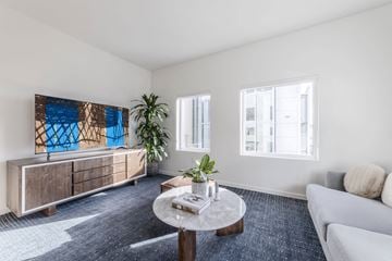 Sacramento apartment for rent - A living room with a grey couch, a coffee table, a plant, and a painting on the wall.