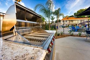West Covina apartment for rent - A large outdoor grill is in the foreground with a patio and pool in the background at Nola 624 Apartments, California, 91790