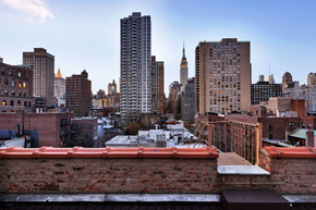 New York triplex for rent - A cityscape with a tall building in the background and a brick wall in the foreground.