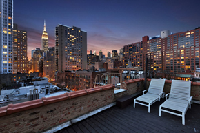 New York triplex for rent - Two chairs are on a balcony overlooking a city skyline.