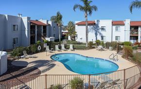 Tucson apartment for rent - A pool surrounded by a fence and chairs in front of a white building.