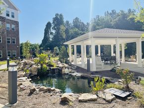 Buford apartment for rent - A gazebo is situated in a garden with a pond and a building in the background.