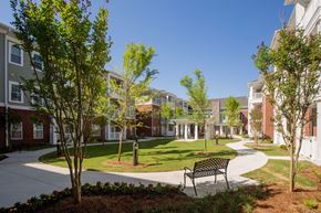 Gainsville apartment for rent - A park with a bench and trees in front of apartment buildings.