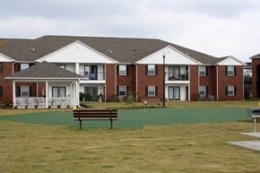 Cartersville apartment for rent - A large building with a white porch and a brown bench in front of it.