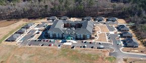 Newnan apartment for rent - A large building with a green roof is surrounded by smaller buildings and a parking lot.