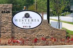 Mableton apartment for rent - A sign for Wisteria Place with a brick wall and flowers.