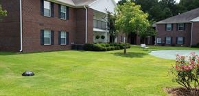 Summerville apartment for rent - A grassy area in front of a brick building with a tree and a flower bed.