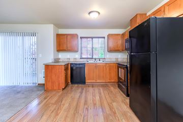 Salem apartment for rent - A black refrigerator is in the corner of a kitchen with wooden floors and cabinets.